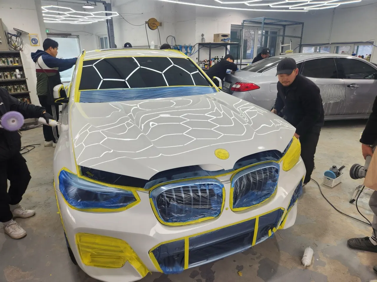 흰색 BMW 주변에서 여러 교육생이 함께 작업하는 실습