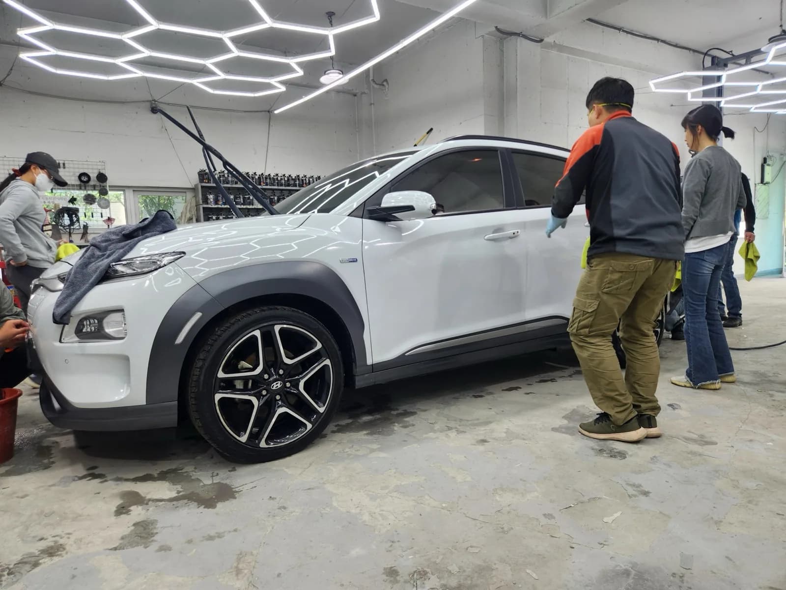 실습장에 세워 둔 흰색 SUV 한 대를 놓고 수강생과 강사가 둘러서서 함께 살펴보는 장면